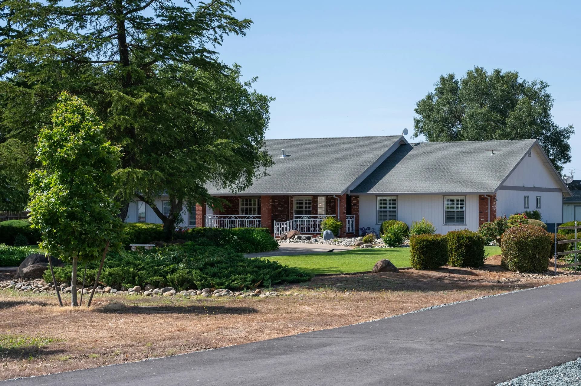 Single-story ranch home with brick and white siding, covered porch, and landscaped yard with mature trees
