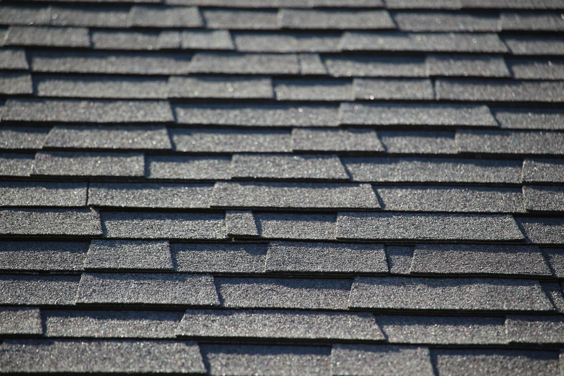 Close-up view of gray asphalt roof shingles in overlapping rows showing texture and shadow detail