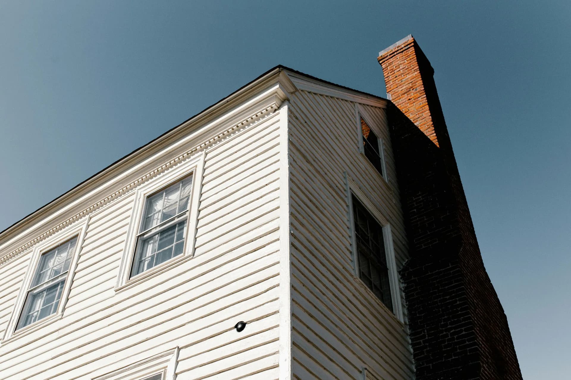White colonial house with red brick chimney photographed from below against blue sky