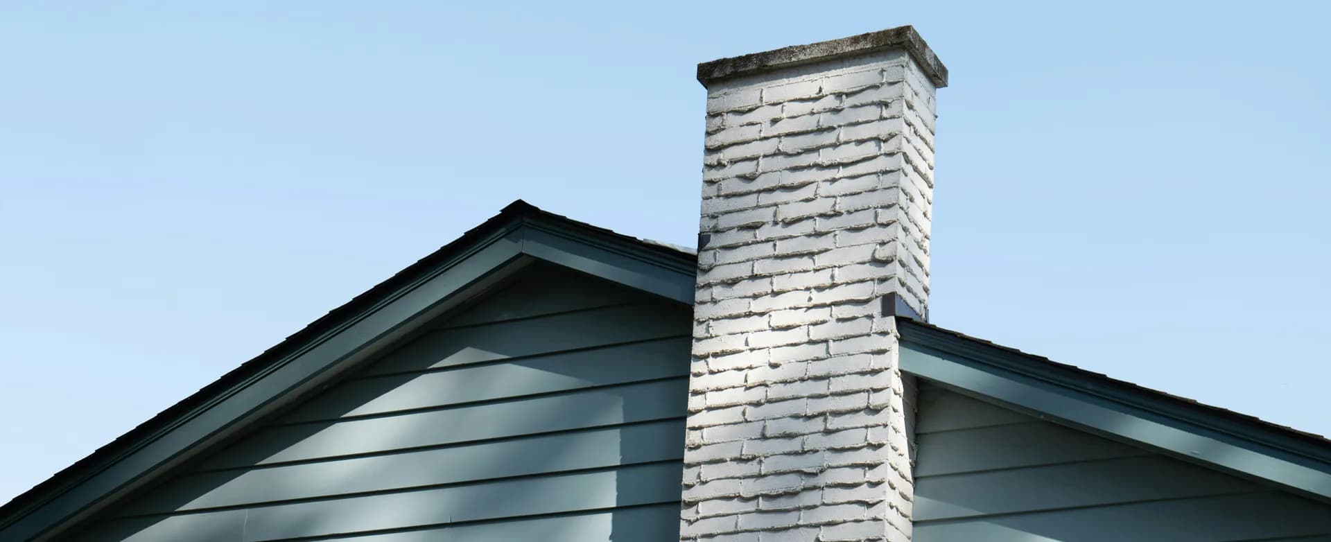White brick chimney on green house roof against blue sky
