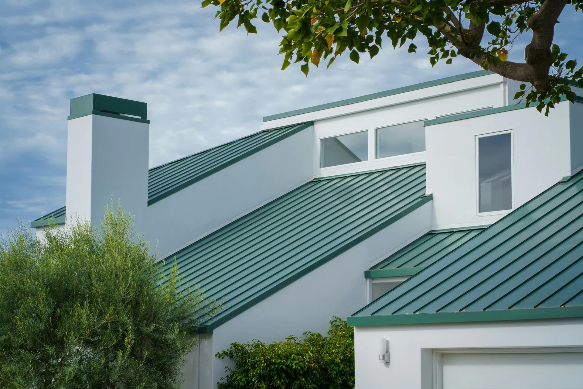 Modern white house with green metal roof and contemporary architecture surrounded by landscaping
