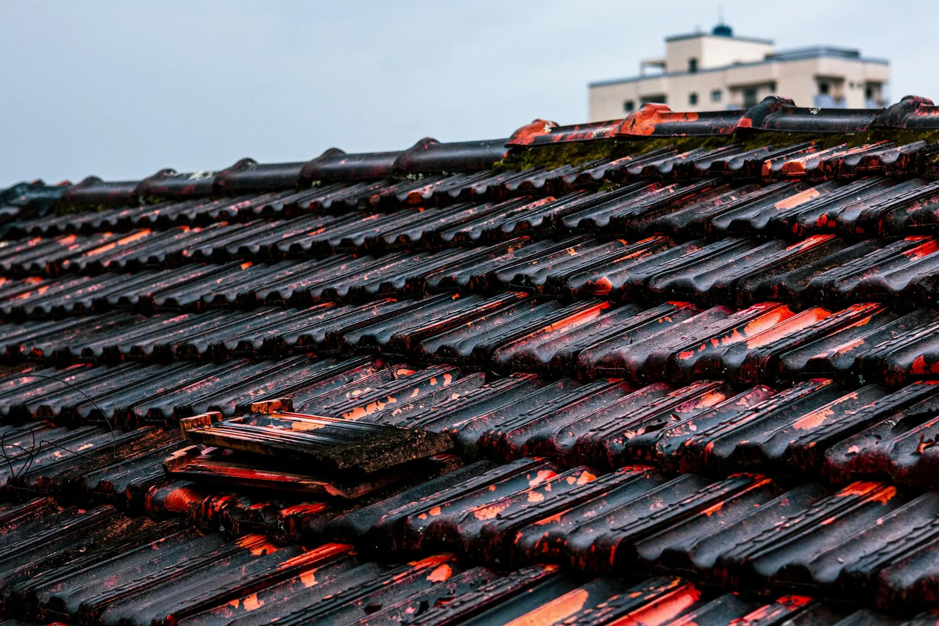 Weathered roof tiles with dramatic red and orange lighting highlighting their textured surfaces and moss growth
