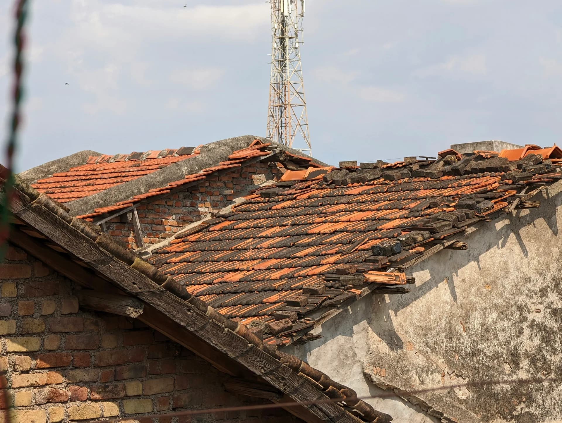 Damaged roof with broken orange tiles and exposed brick wall showing structural deterioration and neglect