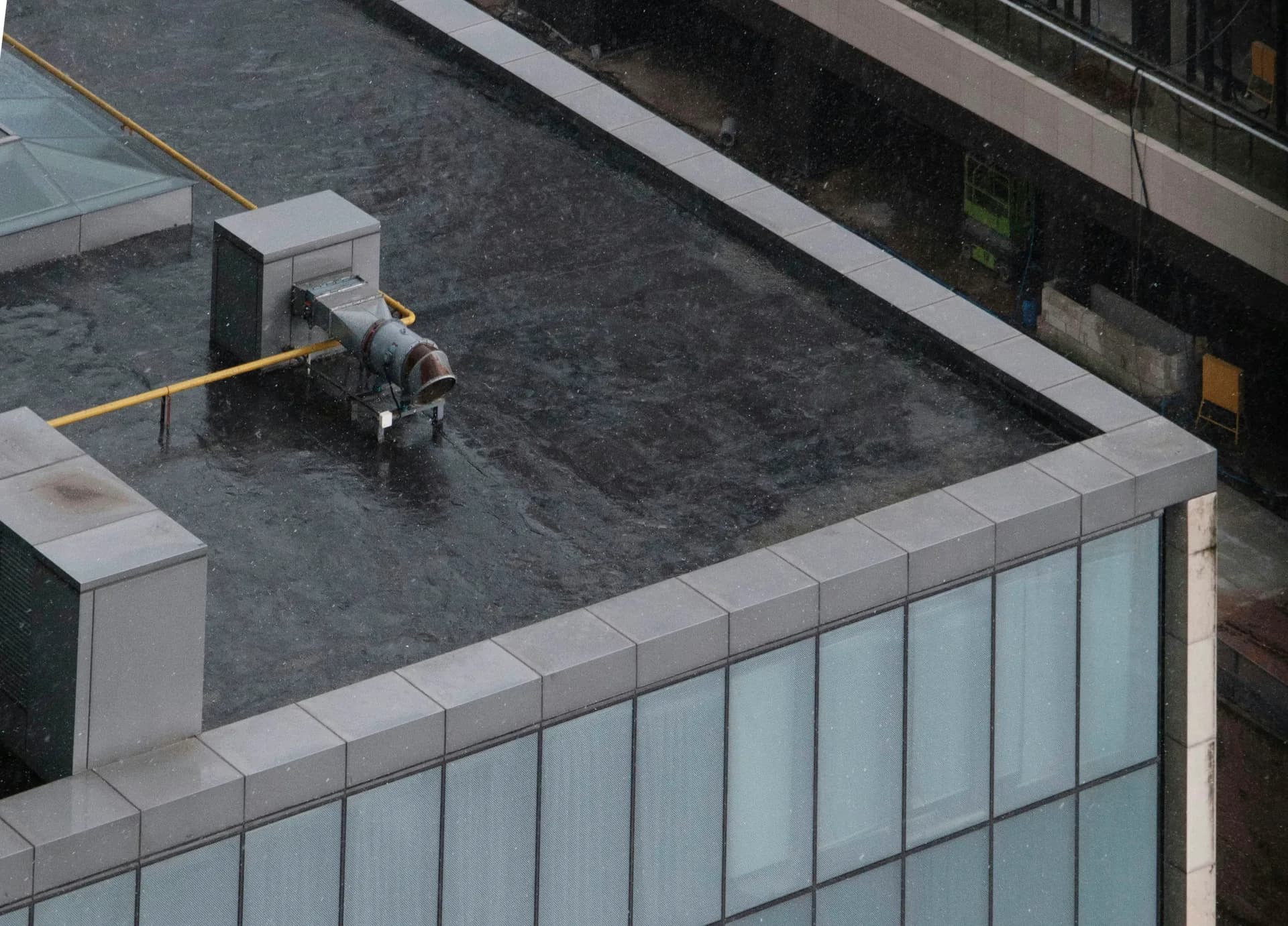 Aerial view of building rooftop with HVAC equipment and concrete parapets overlooking glass facade