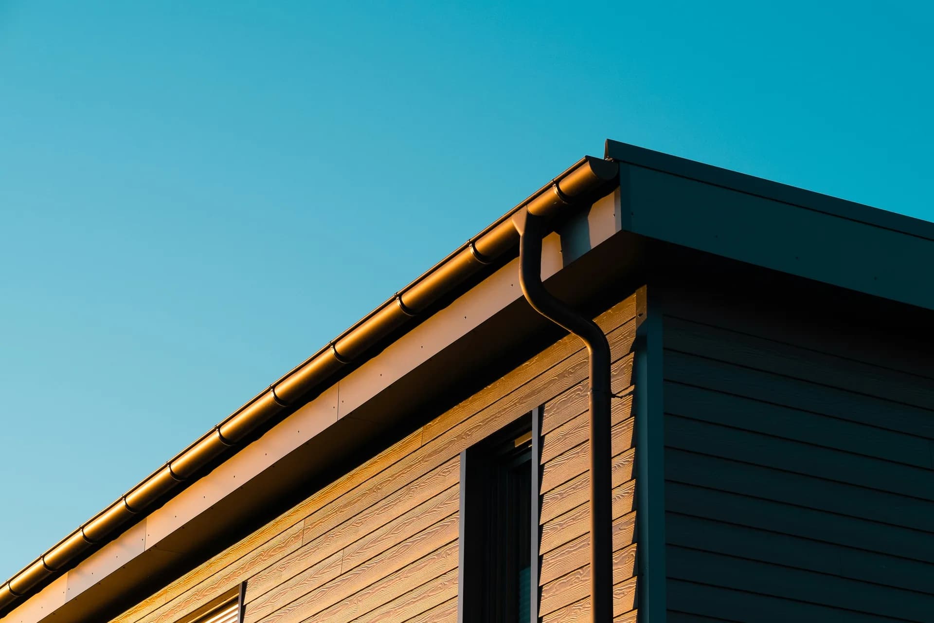 Modern building corner with wood siding, dark metal cladding, and copper gutters against blue sky