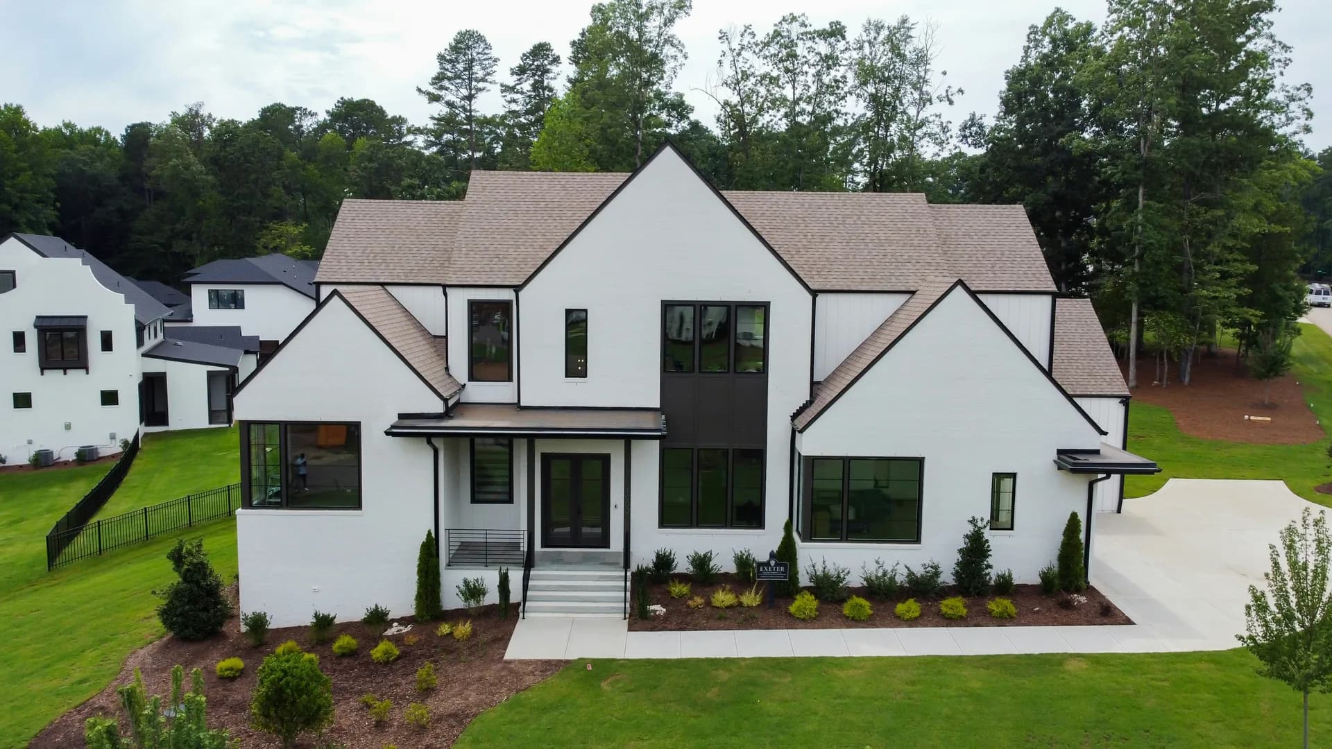 Modern white two-story house with black trim and large windows, aerial view showing manicured lawn and landscaping