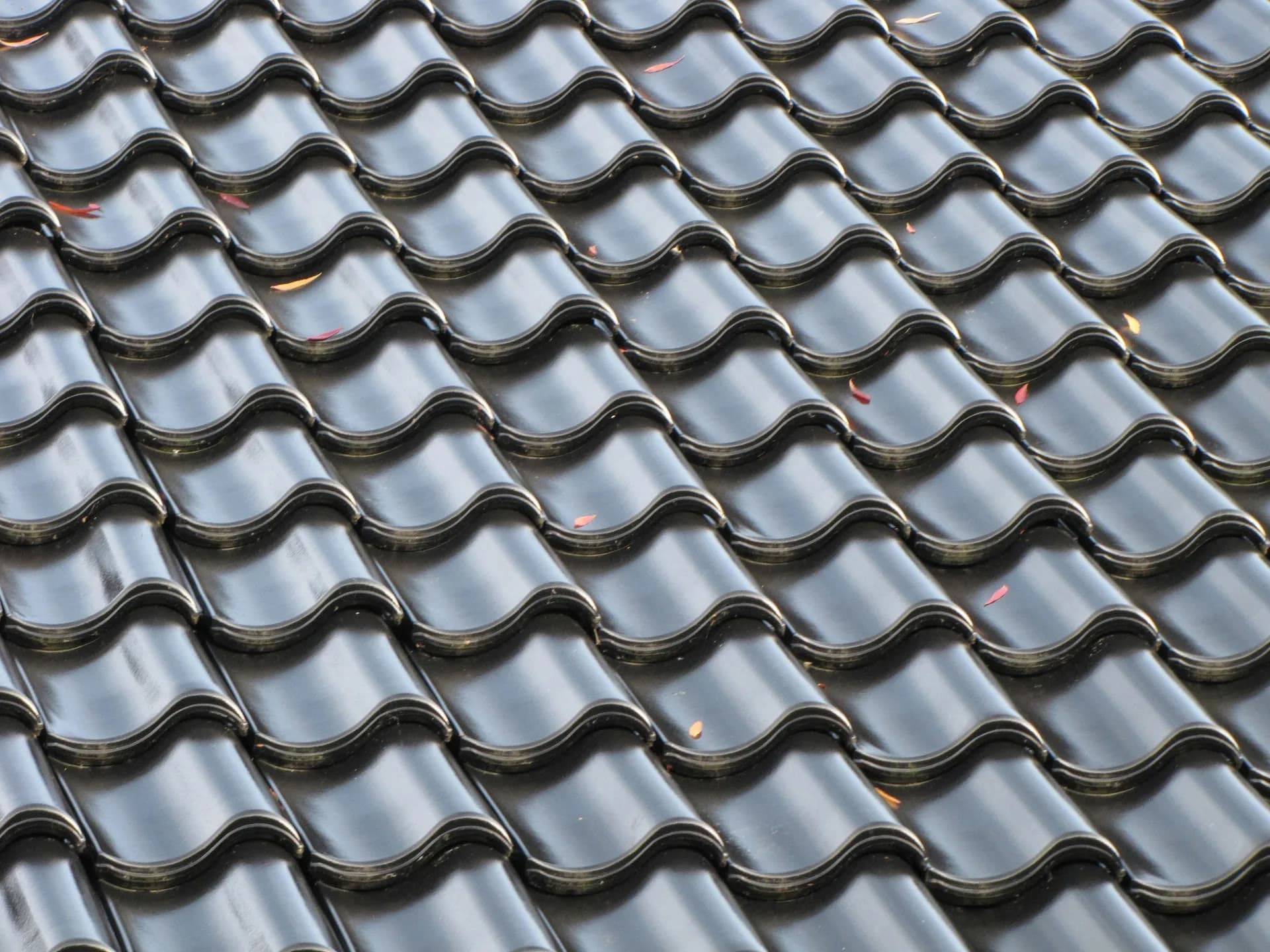 Dark ceramic roof tiles in overlapping rows creating a wave pattern with scattered debris