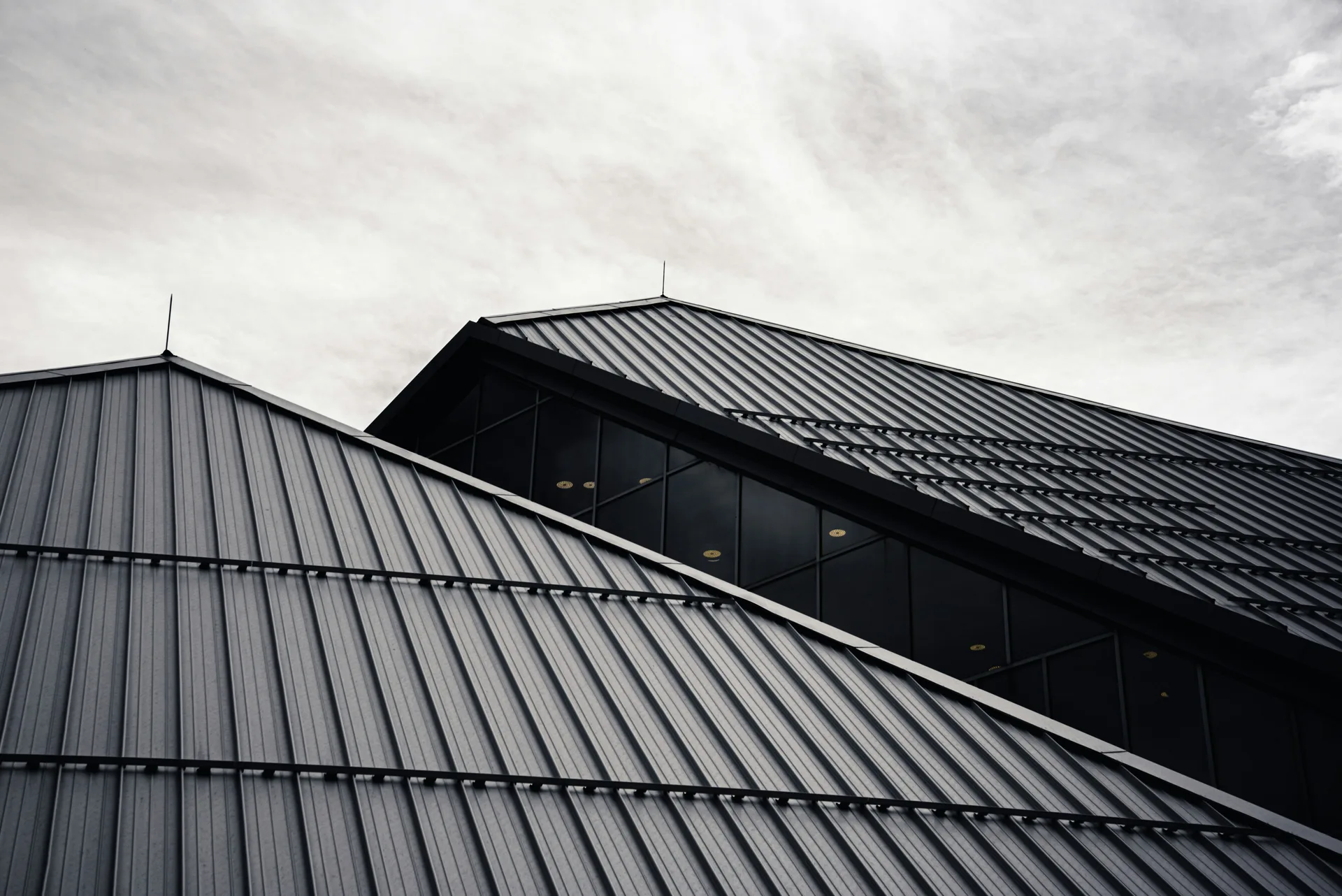 Modern metal roofing with ribbed patterns photographed from below against cloudy sky
