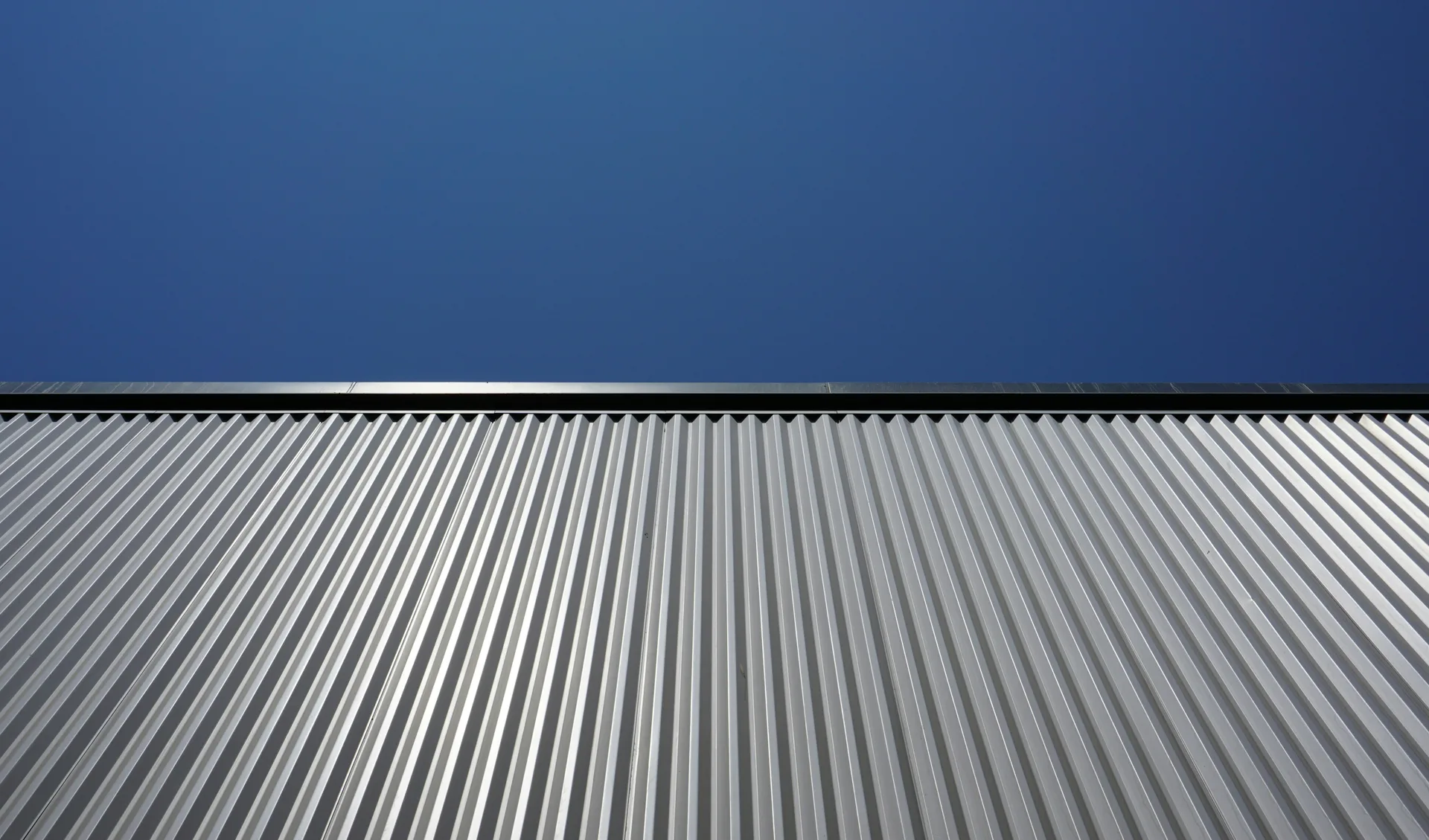 Corrugated metal roof with vertical ridges against blue sky creating geometric pattern