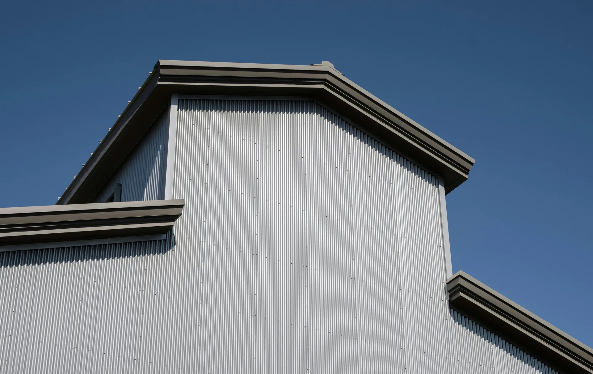 Modern building with white corrugated metal siding and dark roof overhangs against blue sky