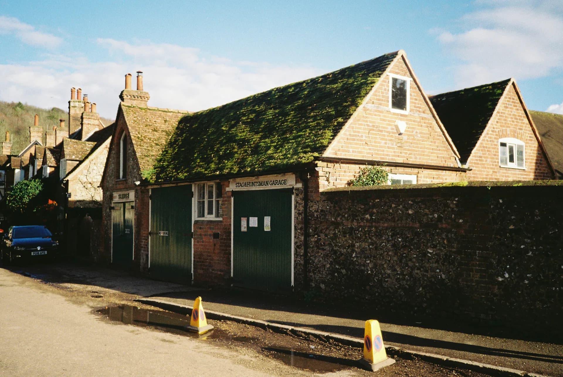 Traditional English village buildings with moss-covered roofs and Staghuntsman Garage with green doors