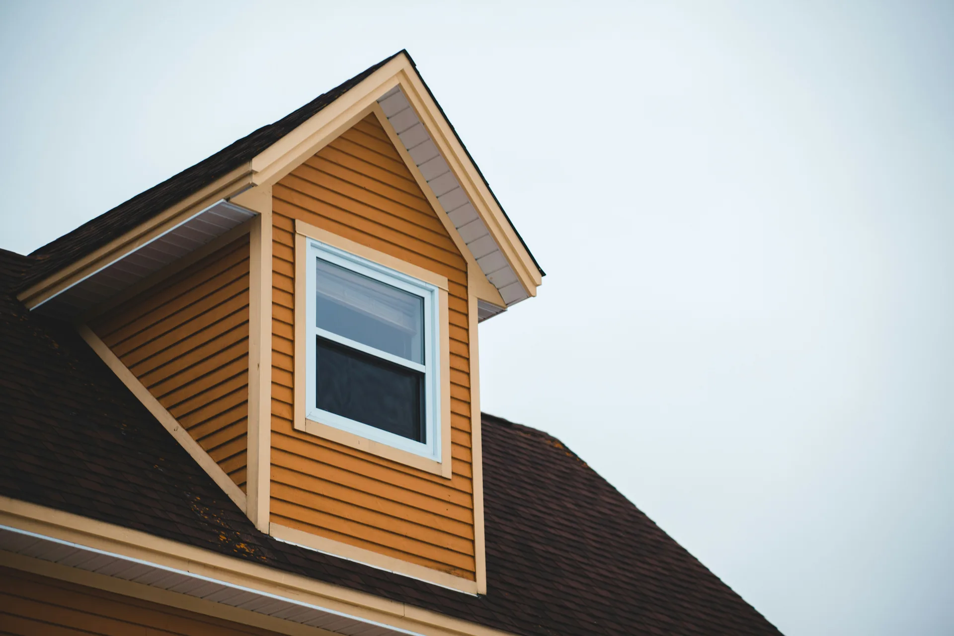 Cedar shake dormer window with white trim on house roof against cloudy sky