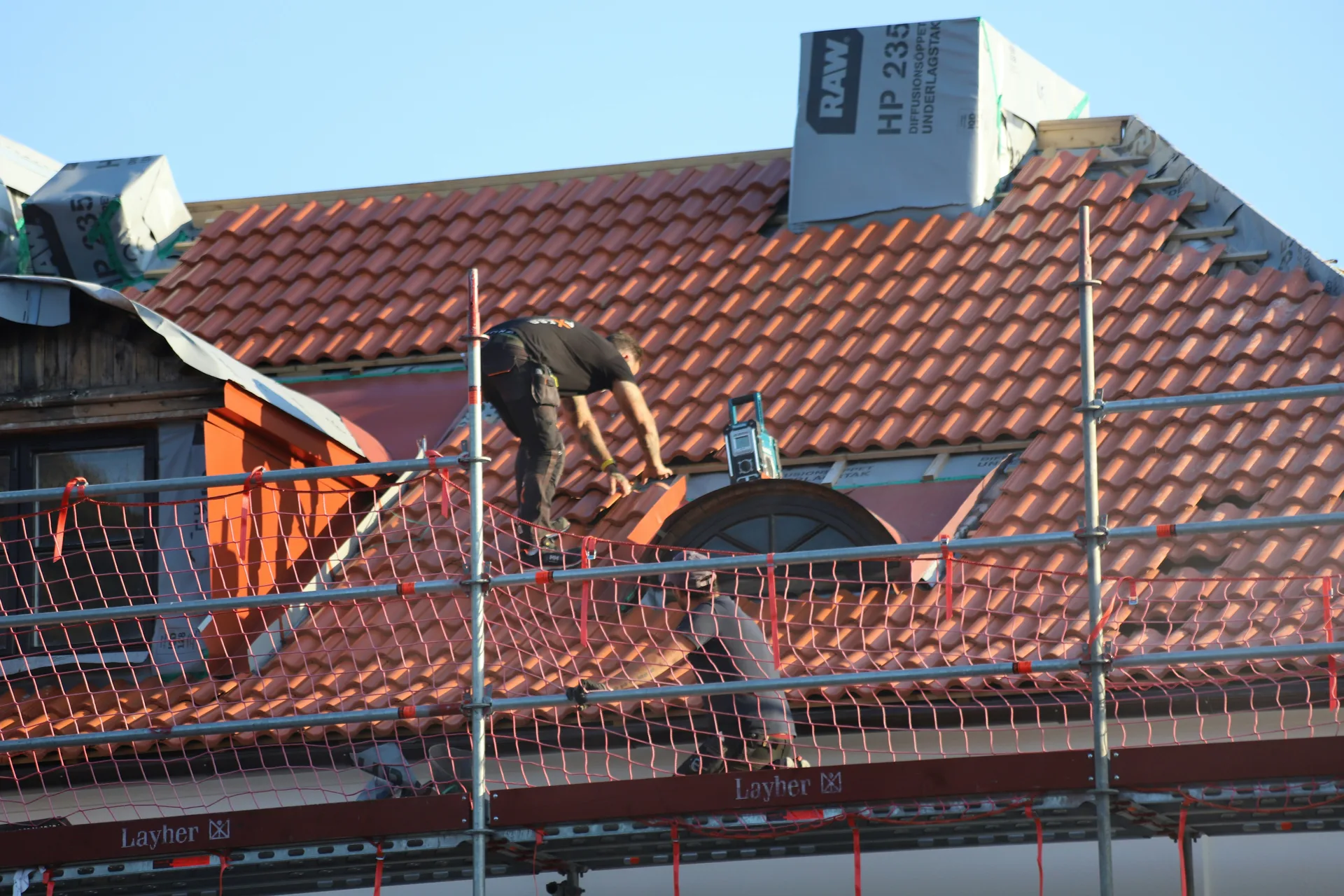 Construction worker installing red clay roof tiles on house with scaffolding