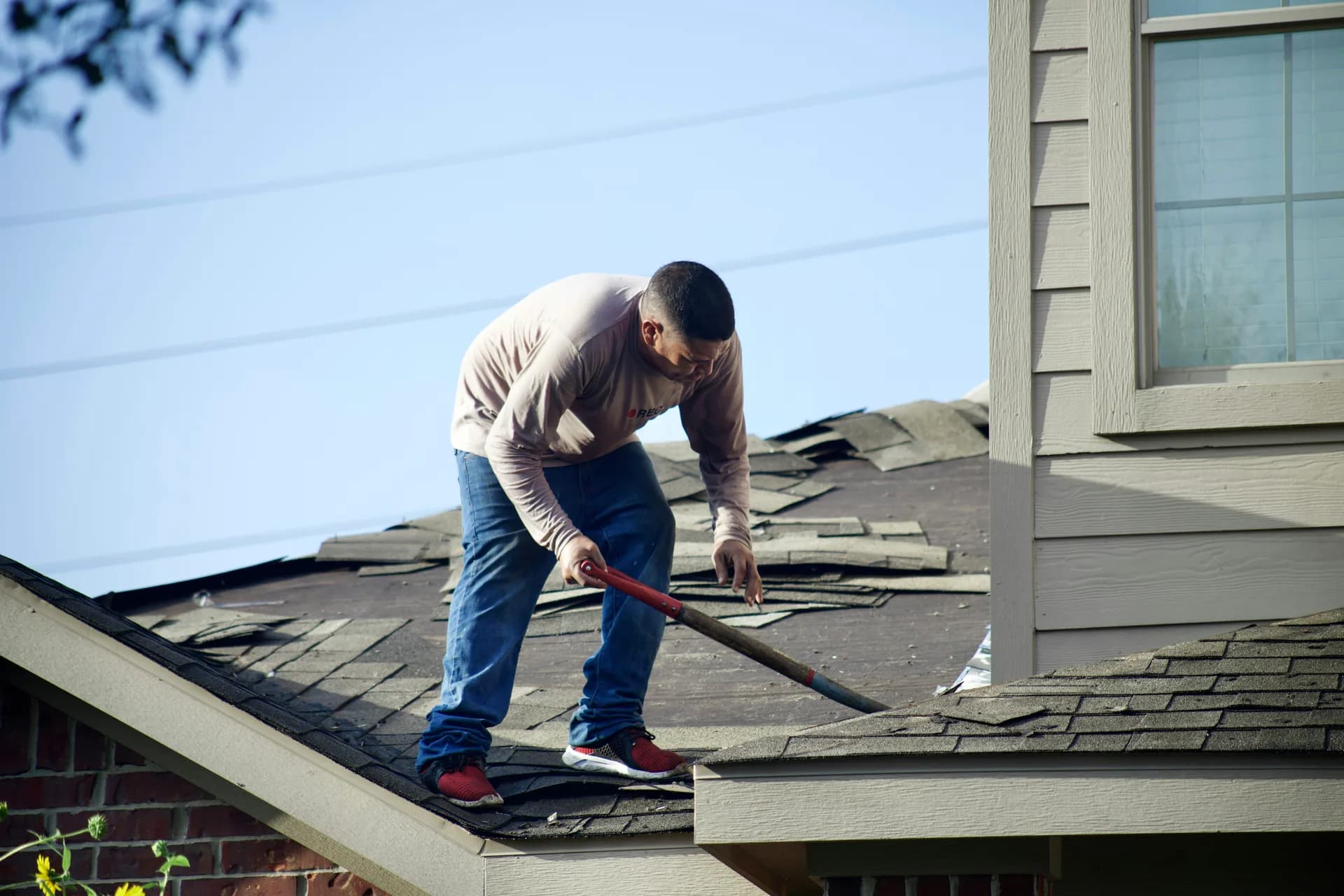 Man repairing damaged roof shingles with crowbar on residential house