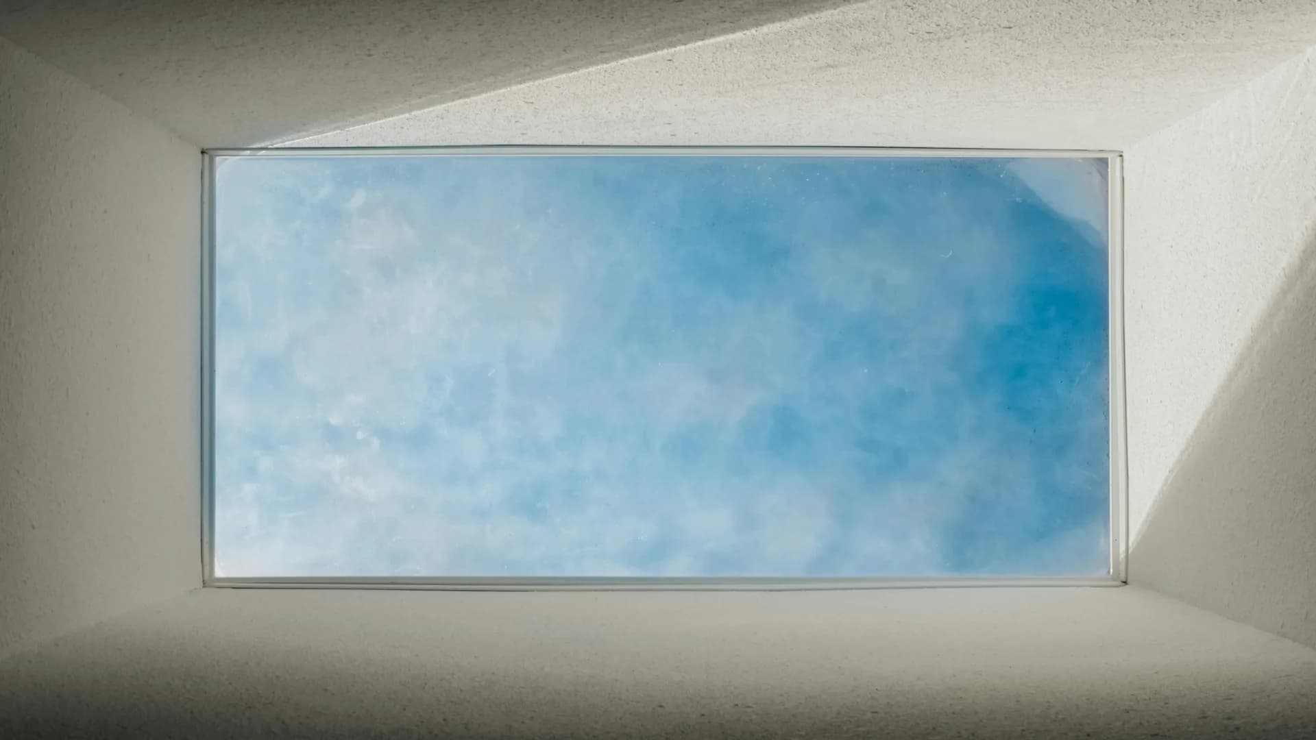 Rectangular skylight in white ceiling showing blue sky with white clouds through the opening