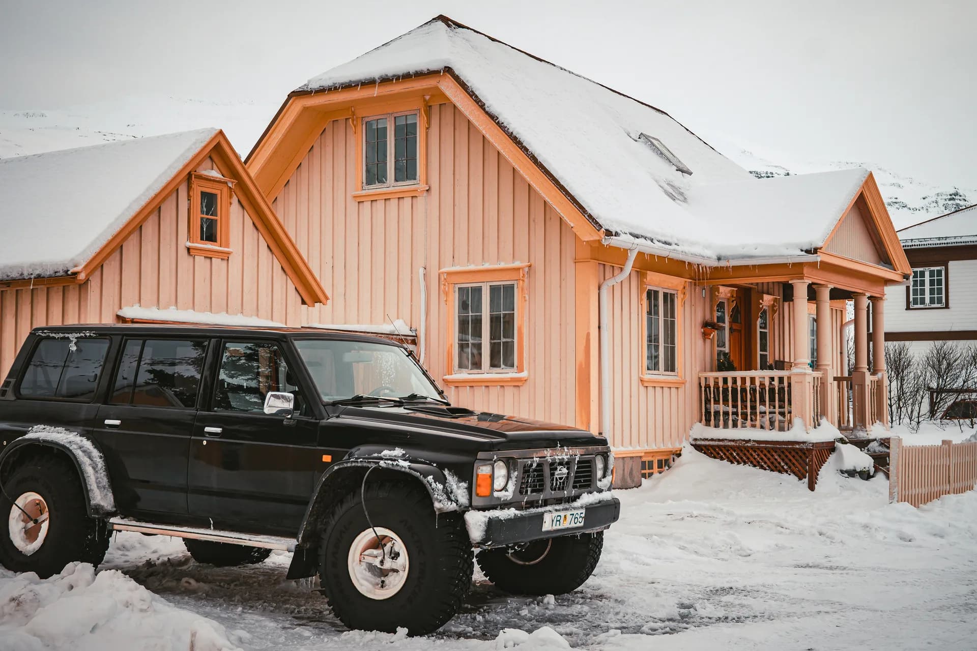 Orange wooden house with snow-covered roof and black vintage SUV parked in snowy driveway during winter