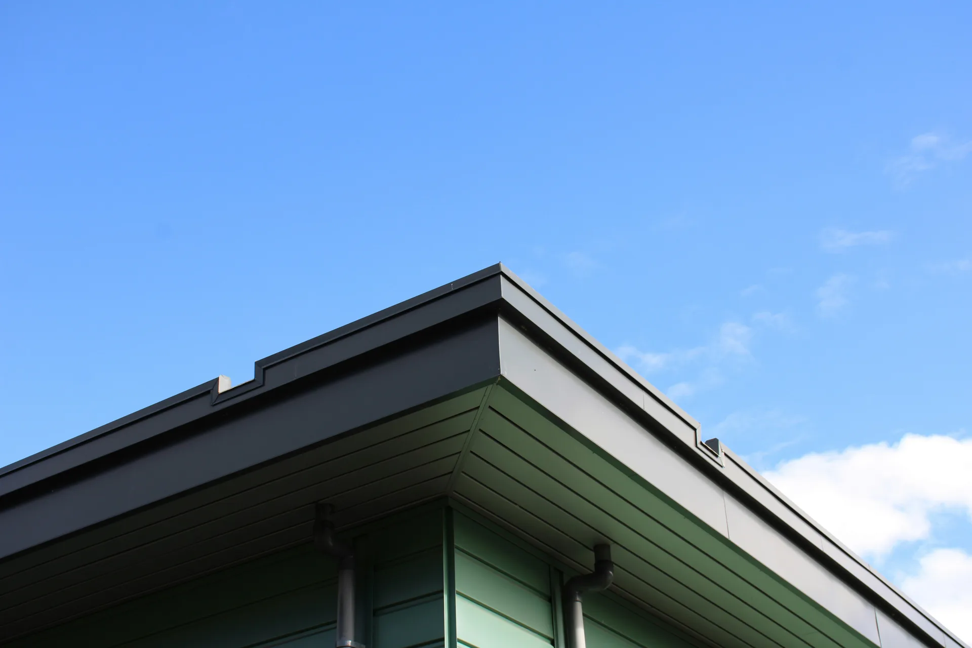 Modern building corner with green siding, white walls, and dark roof trim against blue sky