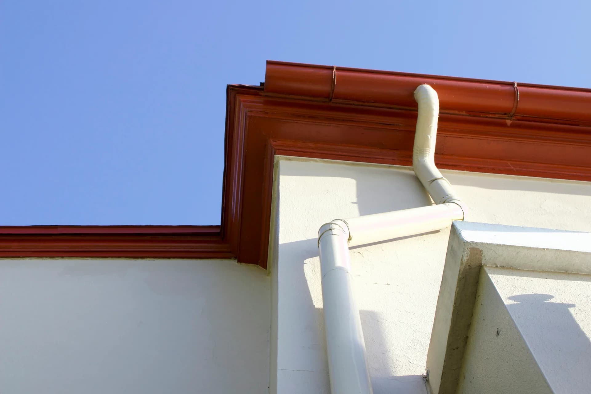 Building exterior corner with white walls, red clay tile roof, and white gutters against blue sky