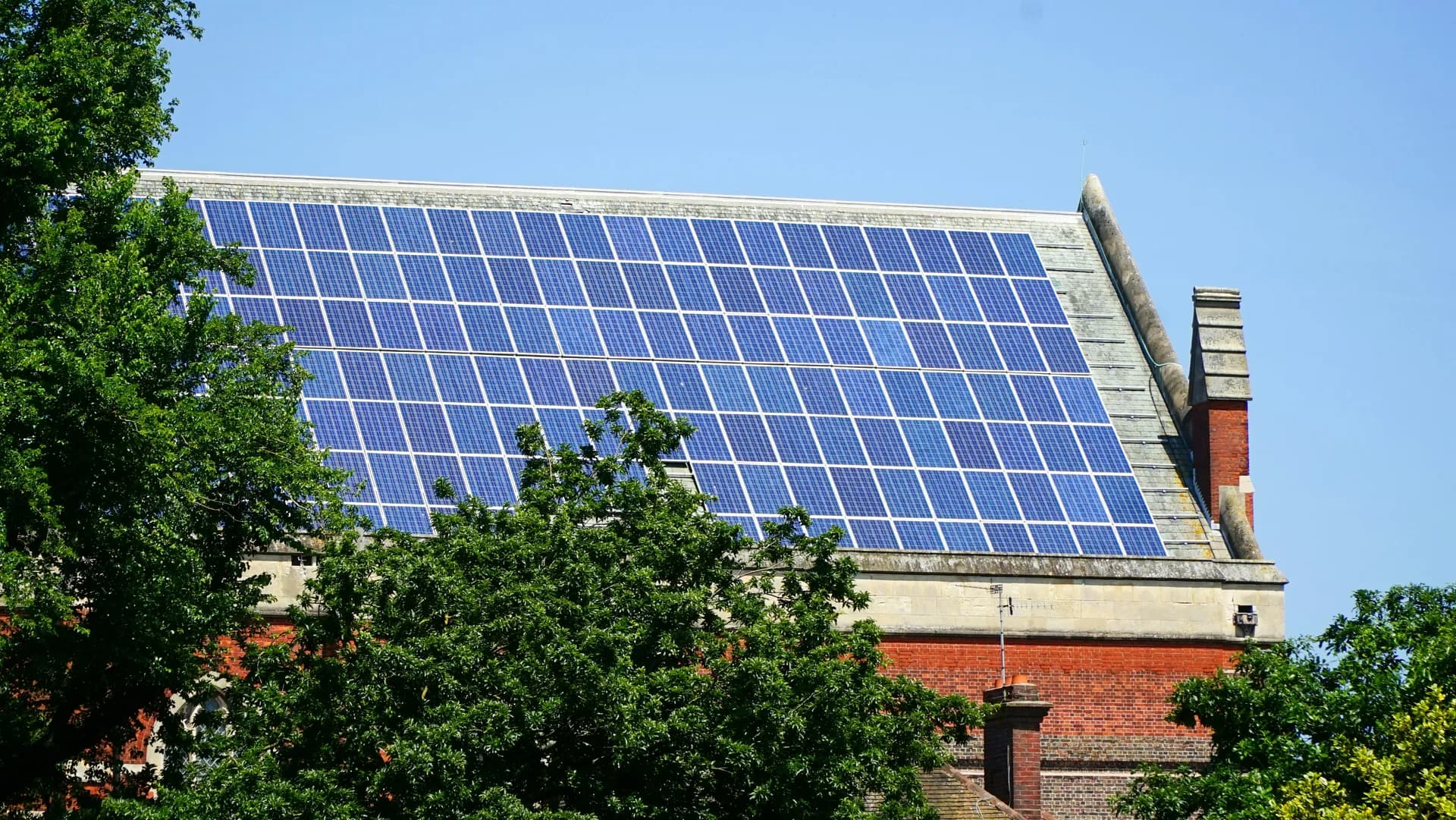 Solar panels installed on roof of brick building with green trees and blue sky