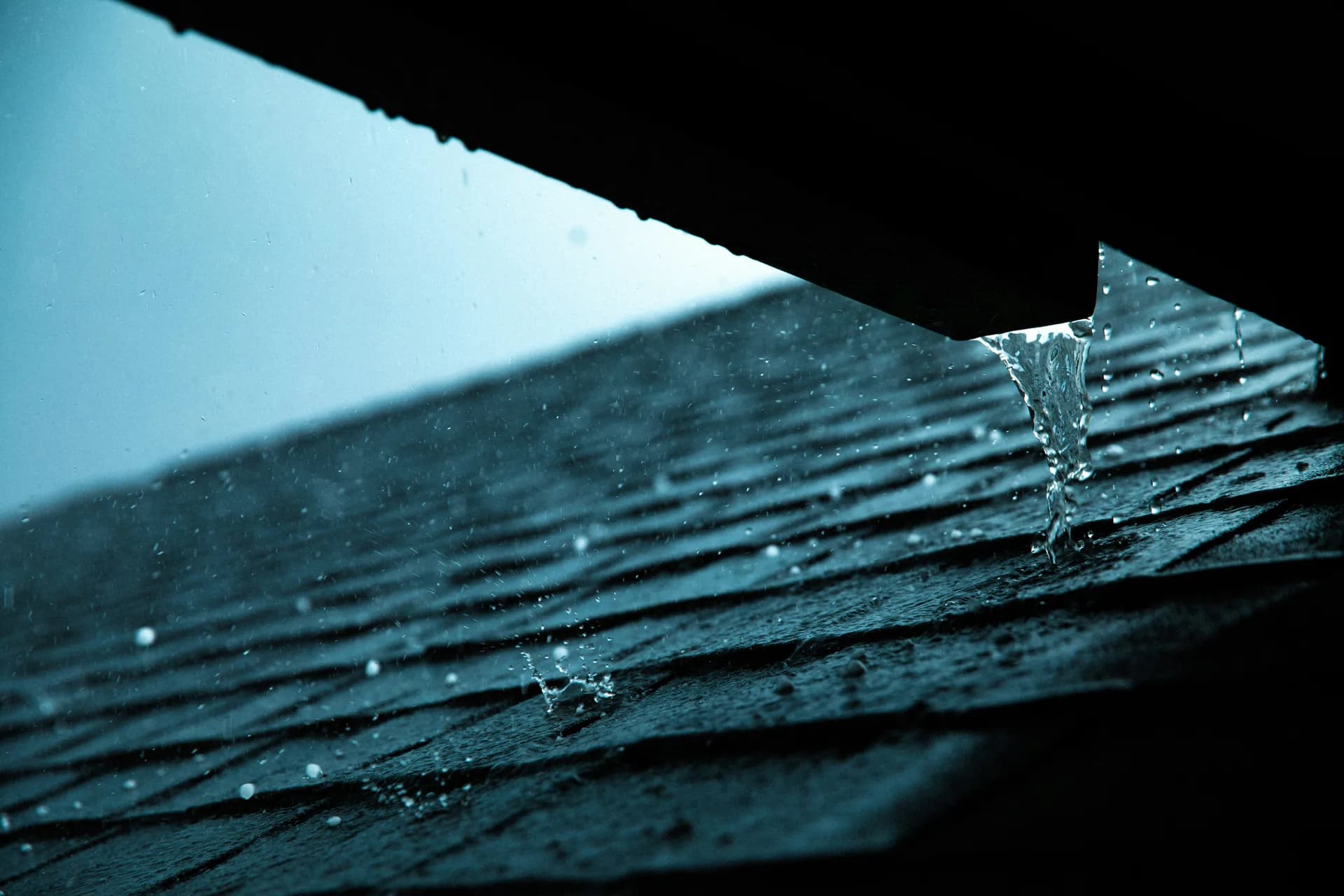 Water dripping from dark wooden roof edge with droplets falling against bright sky