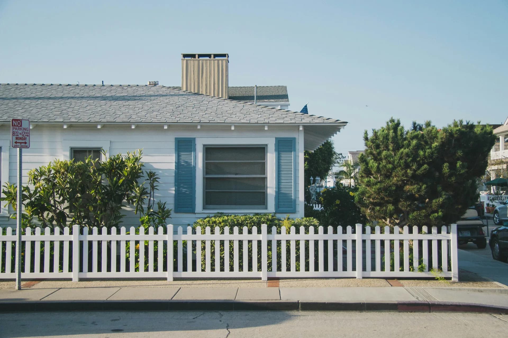 White beach cottage with turquoise shutters behind white picket fence with green landscaping