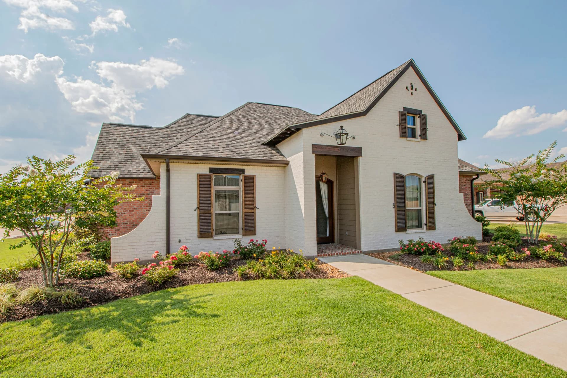 White brick house with brown shutters, covered front porch, and landscaped yard with flowers and green lawn