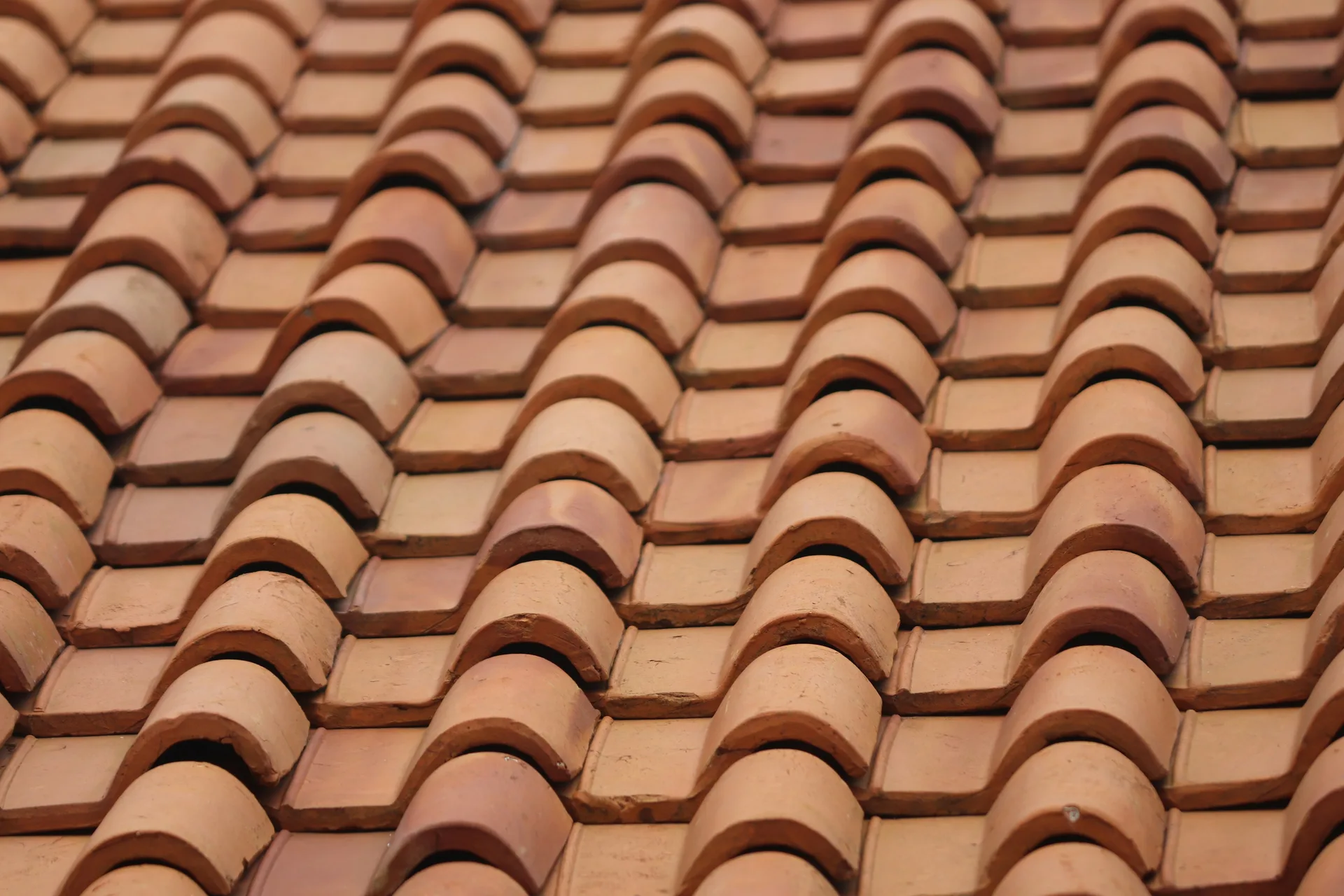 Close-up of overlapping terracotta roof tiles in warm brown and beige tones arranged in curved rows