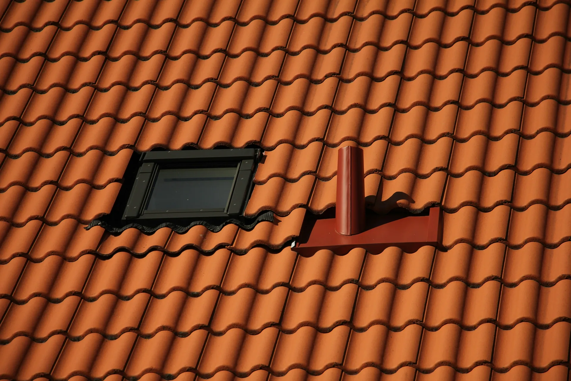 Orange clay tile roof with skylight and ventilation pipe in Mediterranean architectural style
